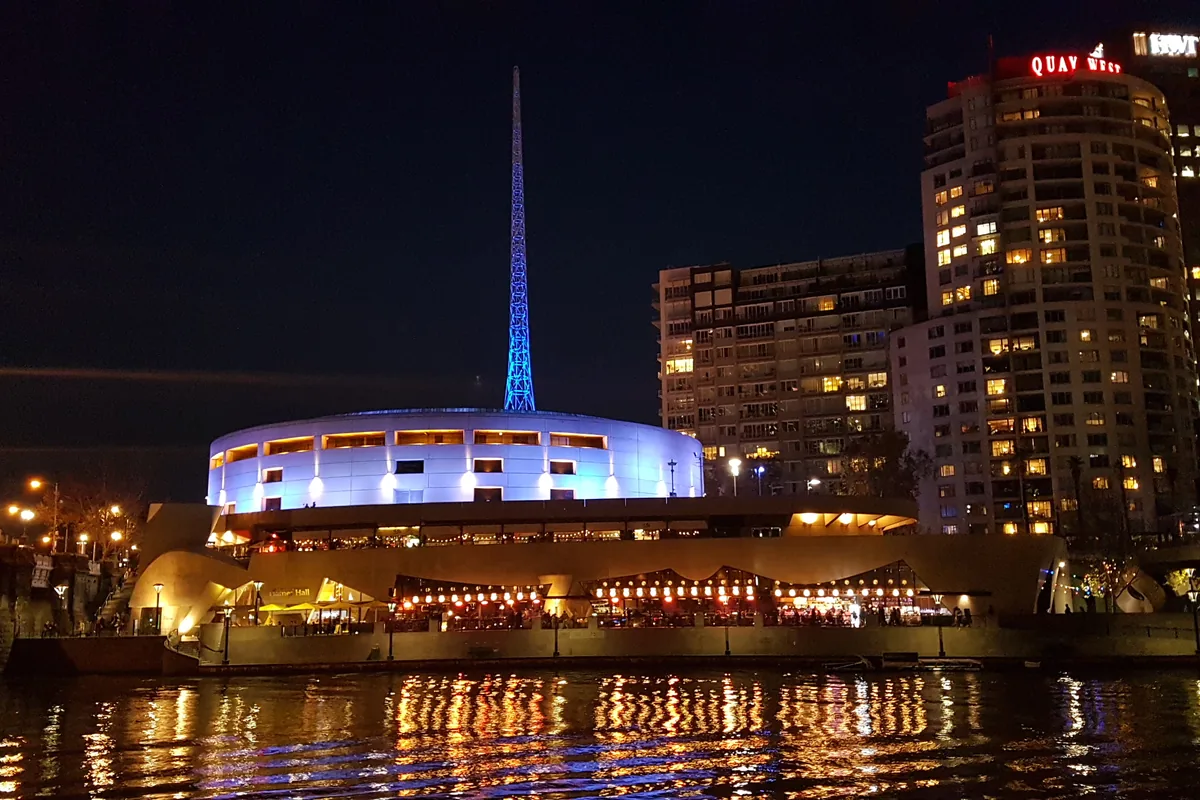 The lit spire and white dome of Arts Centre Melbourne across the Yarra at night.