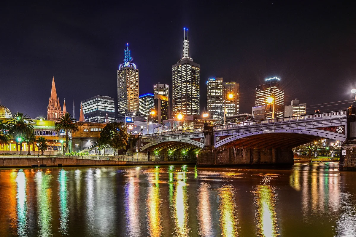 Princes Bridge arching over the Yarra at night with the city towers behind it and colourful reflections in the water.